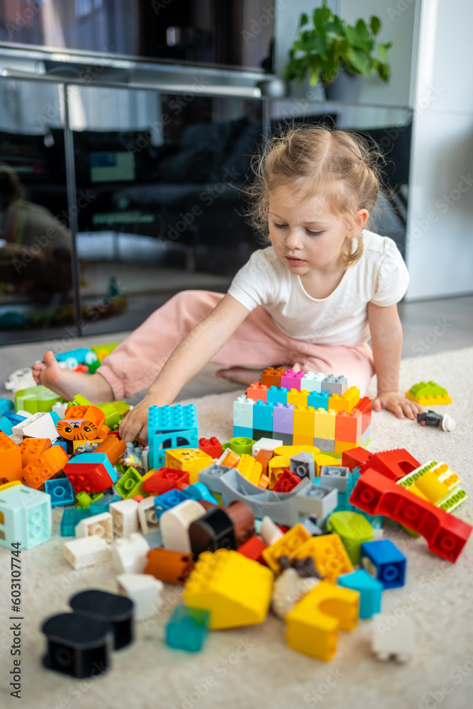 Little girl play with constructor toy on floor in home, educational game, spending leisure activities time concept Little girl play with constructor toy on floor in home, educational game, spending leisure activities time concept