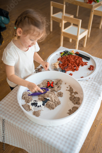 Little girl playing with kinetic sand and toys insect. Sensory development and experiences, themed activities with children, fine motor skills development