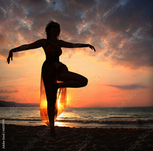 Woman doing yoga exercise on the beach at sunset  silhouette