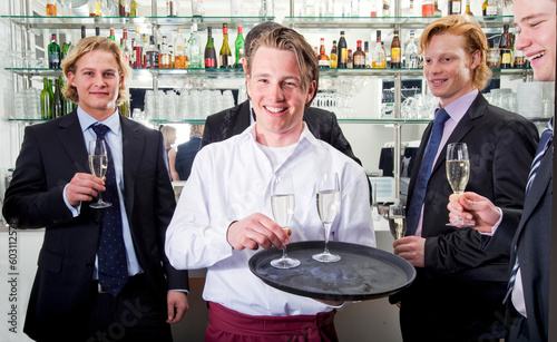 a waiter serving champagne with his customers behind him
