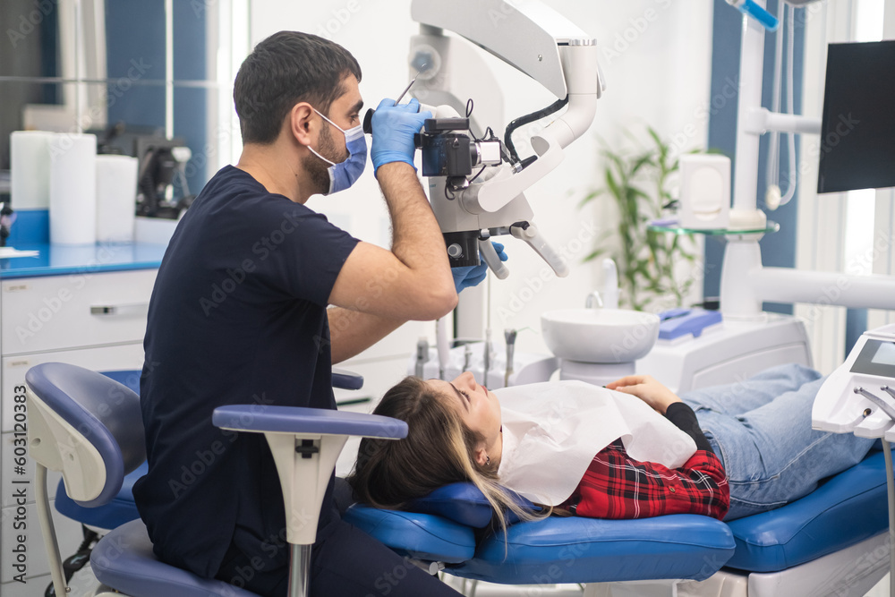 Attentive dentist looks at teeth of young woman through modern dental microscope professional upscale services in contemporary dentistry clinic doctor using innovative equipment Attentive dentist looks at teeth of young woman through modern dental microscope professional upscale services in contemporary dentistry clinic doctor using innovative equipment