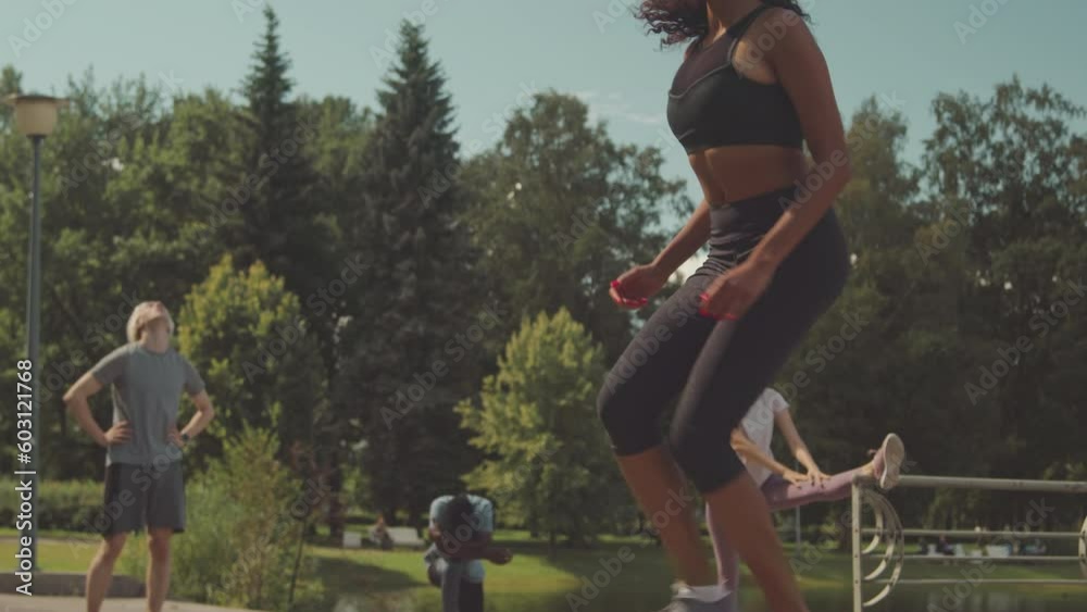 Tilt up slowmo of young fit Biracial woman doing step ups during outdoor boot workout with other athletes in public park on sunny day Tilt up slowmo of young fit Biracial woman doing step ups during outdoor boot workout with other athletes in public park on sunny day