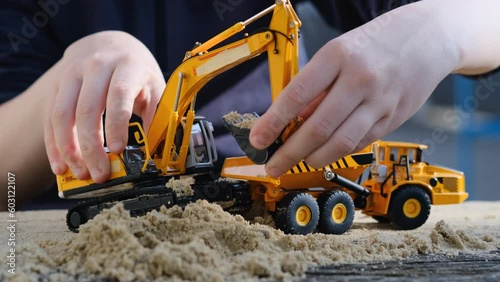 A child plays in the sand with a yellow excavator and a truck. Children's YouTube channel. Construction concept.