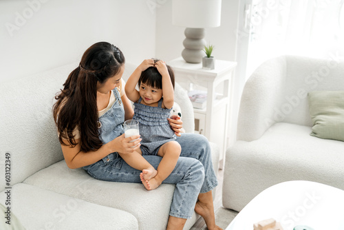 Young nanny sitting on couch serving milk with little girl photo