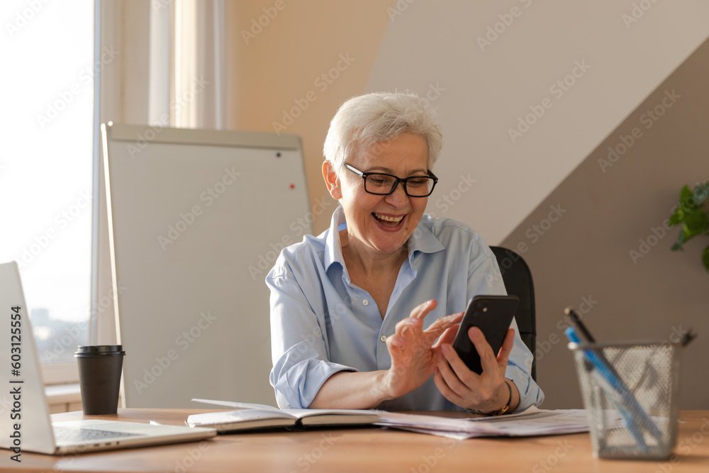 Confident stylish european middle aged senior woman using smartphone at workplace. Stylish older mature 60s gray haired lady businesswoman with cell phone in office. Boss leader using internet apps Confident stylish european middle aged senior woman using smartphone at workplace. Stylish older mature 60s gray haired lady businesswoman with cell phone in office. Boss leader using internet apps