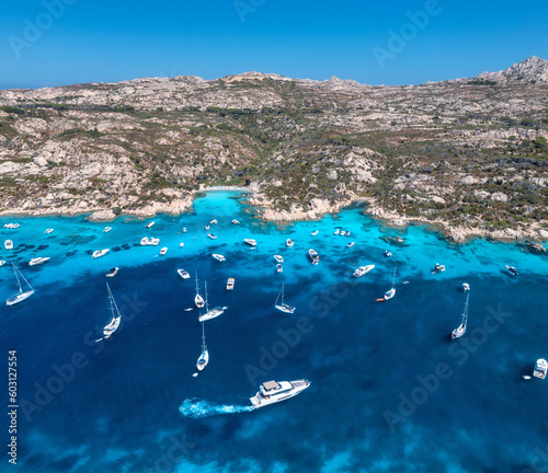 Aerial view of luxury yachts and boats on blue sea at summer sunny day. Travel in Sardinia, Italy. Drone view from above of speed boats, yachts, sea bay, rocky coast, transparent water. Seascape