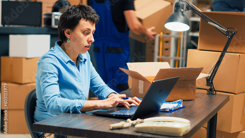 Business owner analyzing boxes with merchandise to ship order to clients, working on products distribution. Woman planning quality control and taking notes on laptop, supply chain management.