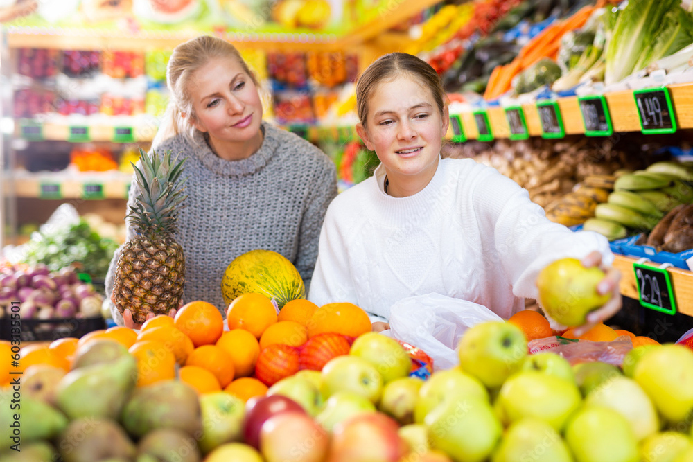Mom and her teen daughter pick pineapple and melon at the grocery supermarket