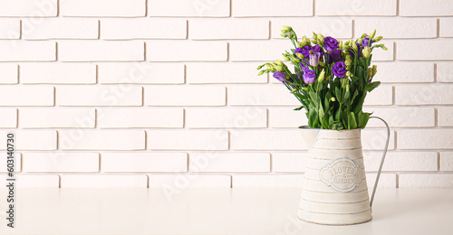 Vase with beautiful eustoma flowers on table near white brick wall. Banner for design