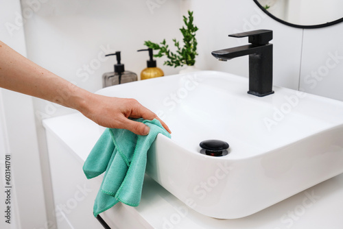 Fototapeta Naklejka Na Ścianę i Meble -  Woman cleaning white washbowl with a black tap in bathroom