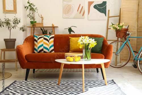 Interior of light living room with cozy brown sofa and narcissus flowers on coffee table