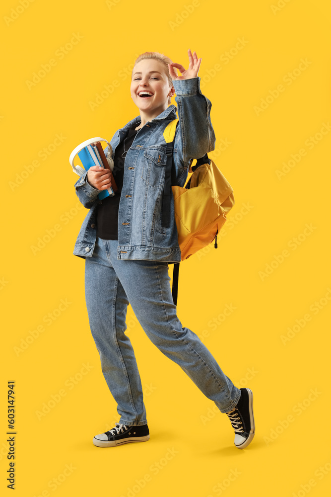 Female student with books and headphones showing OK on yellow background Female student with books and headphones showing OK on yellow background