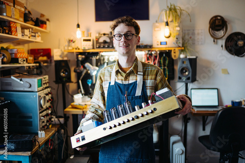Smiling repairman holding valve guitar amplifier in workshop