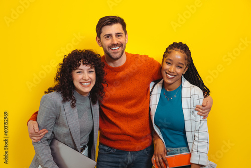 Portrait of happy diverse colleagues posing over yellow wall photo