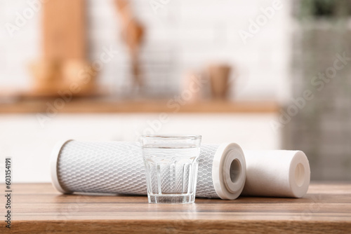 Glass of water with filters on wooden table in kitchen