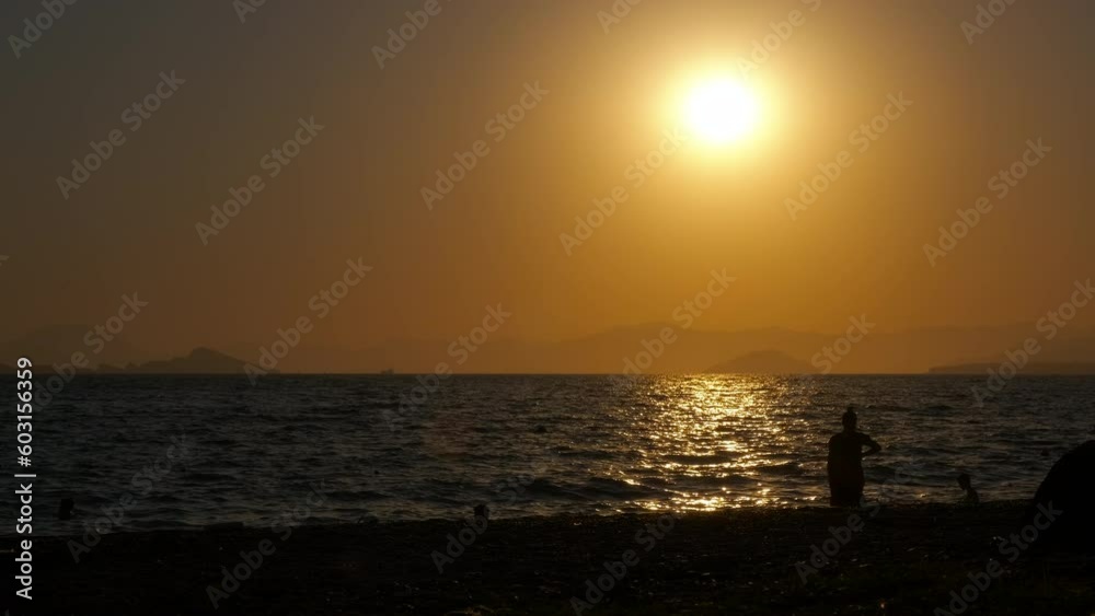 Playing tourist silhouette against ocean. A view of playing people silhouette by the calm sea waves in the evening. A concept of having fun during summer holiday. Playing tourist silhouette against ocean. A view of playing people silhouette by the calm sea waves in the evening. A concept of having fun during summer holiday.