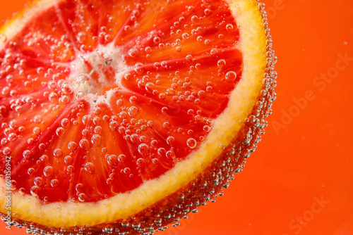 Blood orange slice in water with bubbles on red background photo