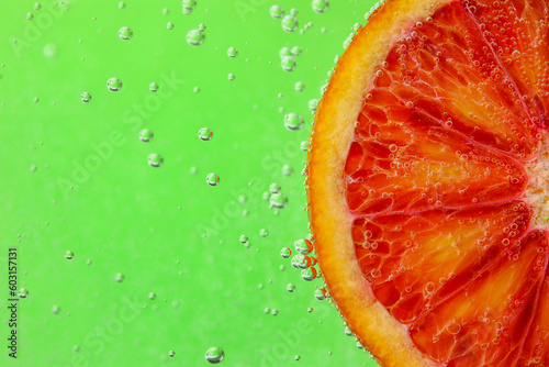 Blood orange slice in water with bubbles on green background