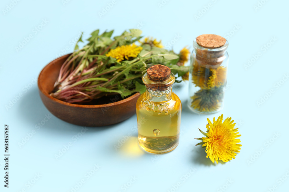 Bottles with cosmetic oil and bowl of dandelion flowers on blue background Bottles with cosmetic oil and bowl of dandelion flowers on blue background