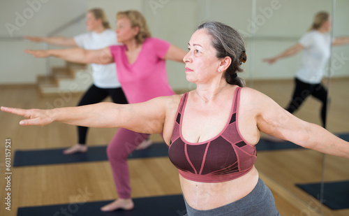 Portrait of mature active woman practicing yoga in group, making stretching asana