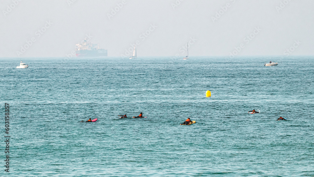 A group of surfers paddling in the middle of the ocean to touch the yellow buoy while they wait for funny waves to do sport 