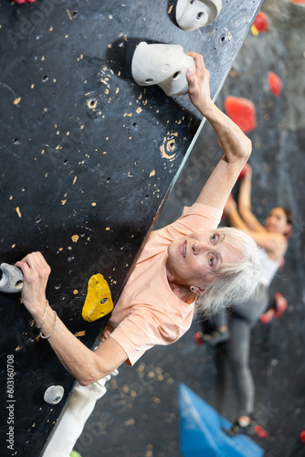 elderly active female pensioner reached top of bouldering wall. active pastime in gym on weekends