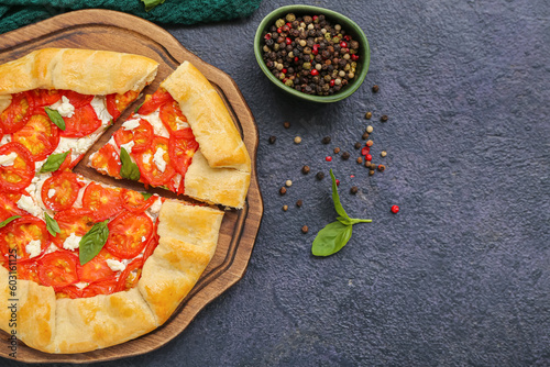 Board with tasty tomato galette and basil on dark background