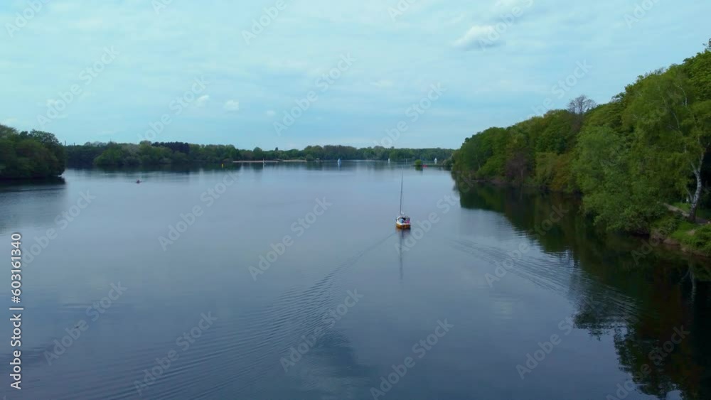 Drone shot over Unterbacher See Lake in Dusseldorf, Germany. Beautiful blue fresh lake water and many green trees and bushes on the coast with beaches and boats sailing under the spring blue sky Drone shot over Unterbacher See Lake in Dusseldorf, Germany. Beautiful blue fresh lake water and many green trees and bushes on the coast with beaches and boats sailing under the spring blue sky
