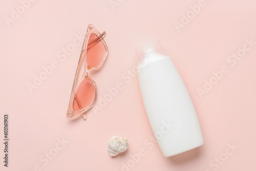 Bottle of sunscreen cream with sunglasses on pink background