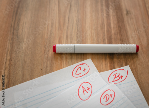 Different grades school paper marked in red ink over a wood desktop.