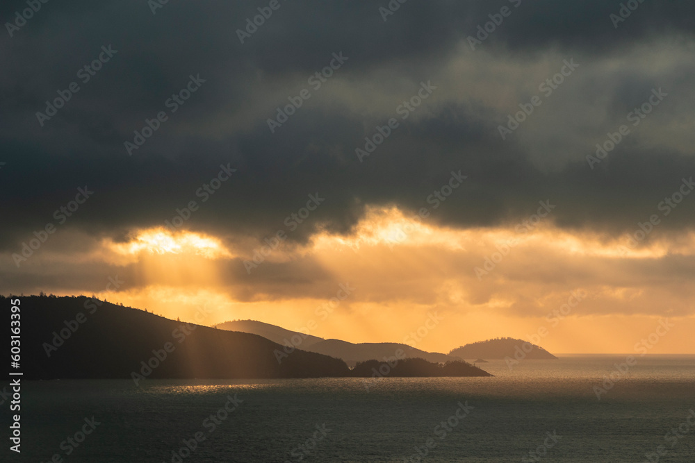 A tropical landscape with the sun breaking through clouds onto the ocean at Hamilton Island, Australia
