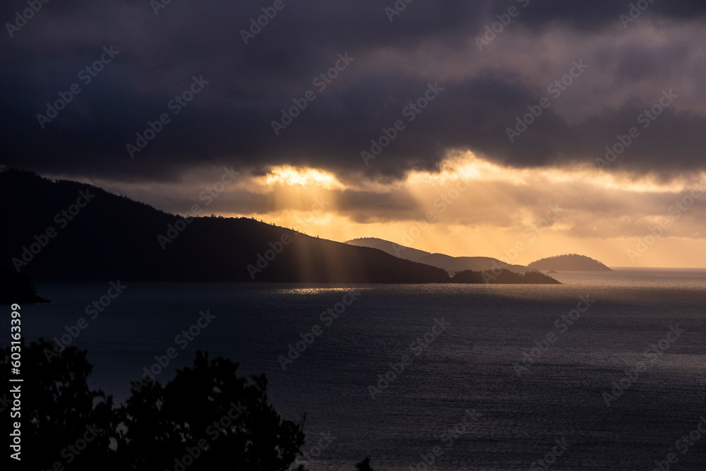 A tropical landscape with the sun breaking through clouds onto the ocean at Hamilton Island, Queensland, Australia
