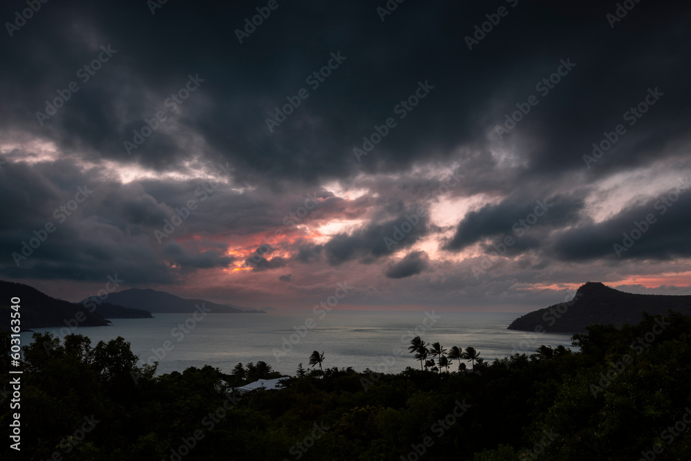 A beautiful tropical landscape with a warm morning sunrise through a dramatic cloudy sky
