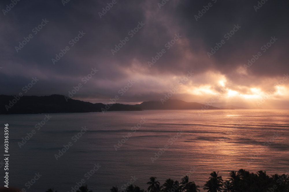 A tropical landscape with the sun breaking through clouds onto the ocean