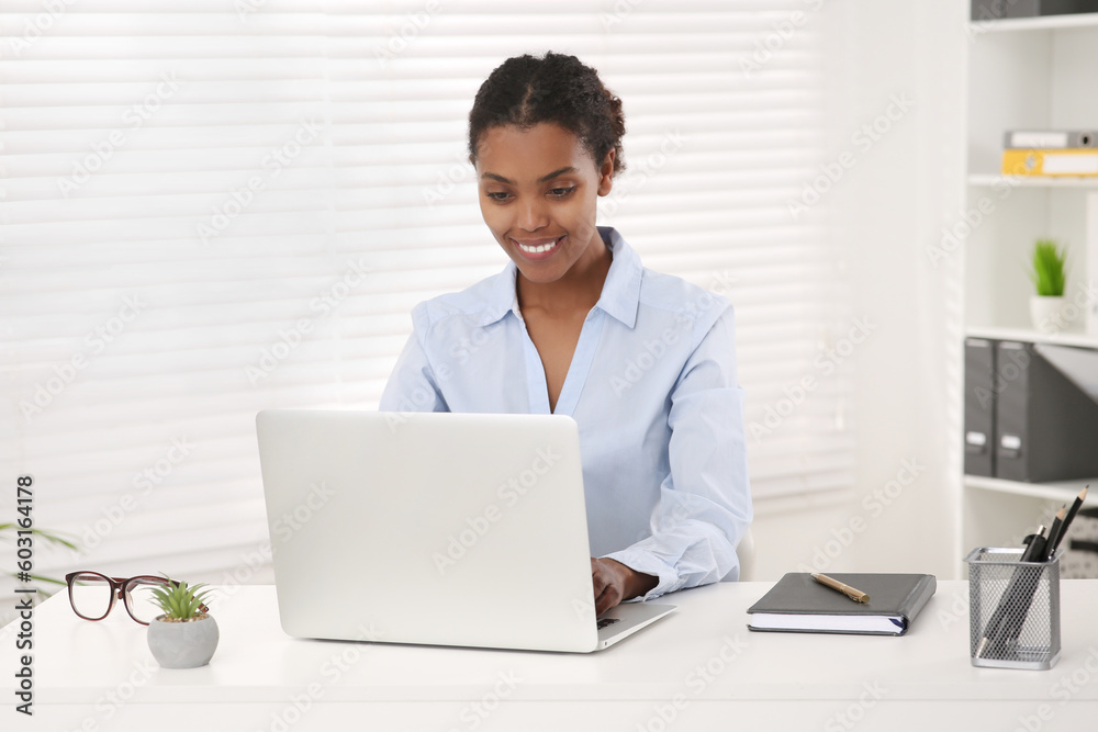Smiling African American intern working on laptop at white table in office Smiling African American intern working on laptop at white table in office