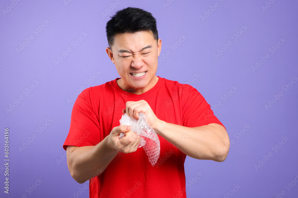 Emotional asian man with bubble wrap on purple background Emotional asian man with bubble wrap on purple background