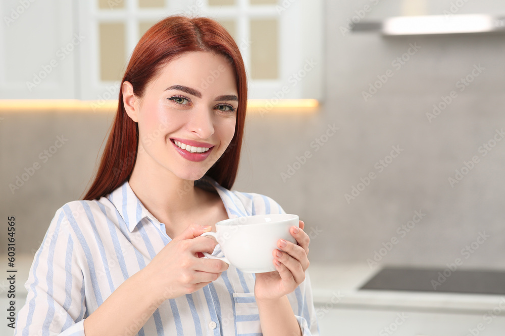 Beautiful woman with red dyed hair holding cup of drink in kitchen, space for text Beautiful woman with red dyed hair holding cup of drink in kitchen, space for text