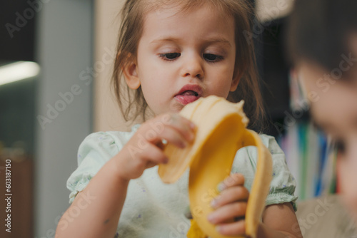 Happy little baby girl eating banana at home. Little girl eating banana. Healthy food.