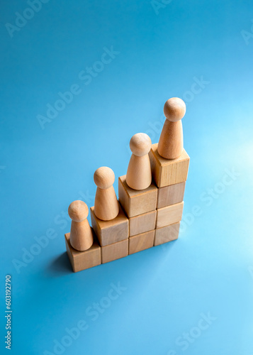 Leadership with business goal and success concept. Wooden figures, as people standing on a growth graph chart steps arranged by wood cube blocks isolated on blue background, vertical style.