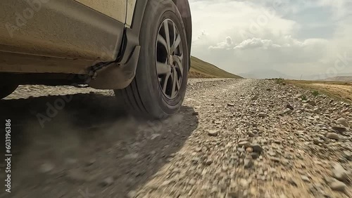 Close-up of a car driving down a dirt, rocky road, creating dust. View of the right front wheel of an SUV car in motion. Traveling by car in Kyrgyzstan. An exciting road trip.