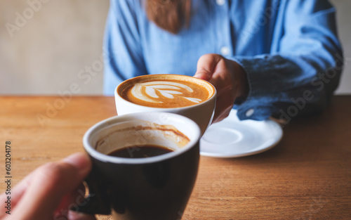 Closeup image of a couple people clinking coffee cups together in cafe