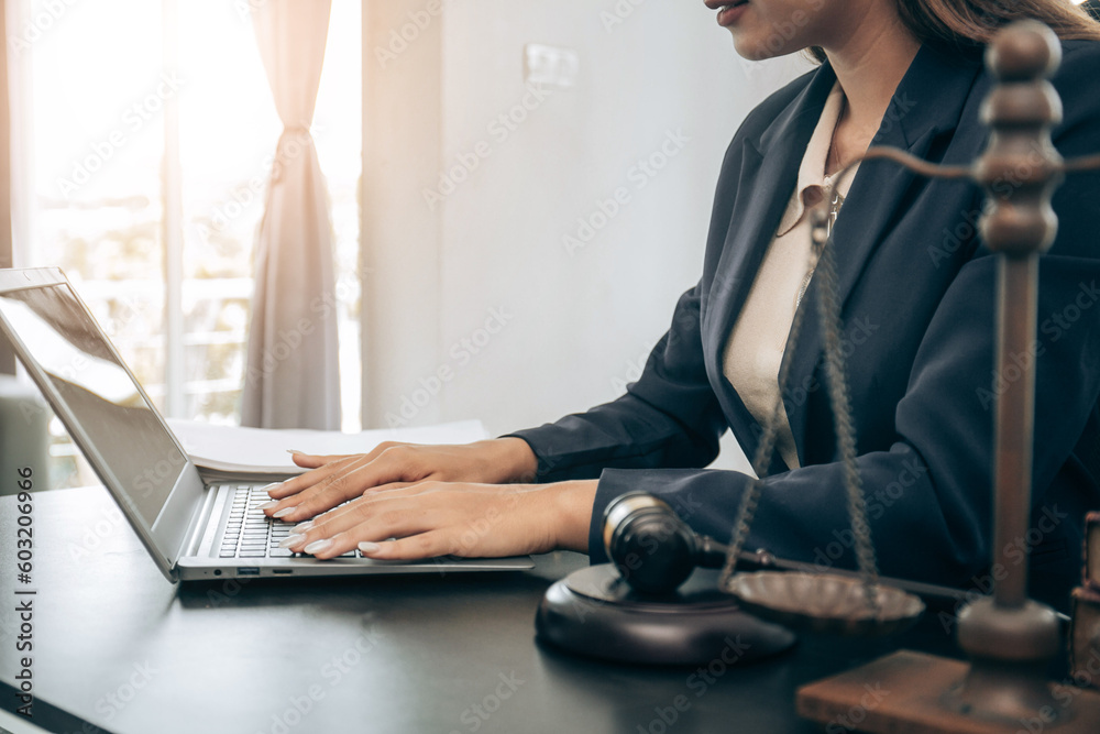 Beautiful young woman lawyer sitting in front of laptop in room with documents and smartphone with empty hammer and scale next to it justice and legal concept Beautiful young woman lawyer sitting in front of laptop in room with documents and smartphone with empty hammer and scale next to it justice and legal concept