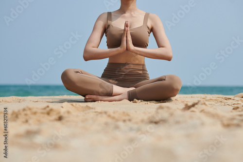 Cropped image of young woman in sports bra and leggings meditating on beach
