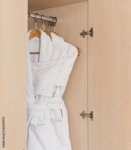 A white bathrobe hangs on a hanger. Vertical photo. Close-up. Selective focus.
