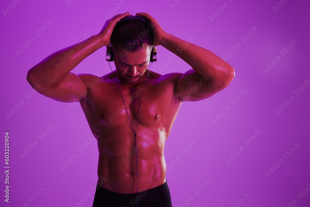 Man wearing headphones athletic physique bodybuilder nude torso abs full-length, fitness classes, purple colored light. Advertising, sports, active lifestyle, competition, challenge concept. Man wearing headphones athletic physique bodybuilder nude torso abs full-length, fitness classes, purple colored light. Advertising, sports, active lifestyle, competition, challenge concept.