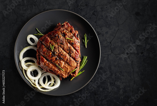 Fotografia Grilled ribeye beef steak with rosemary and marinated onion on a black stone table