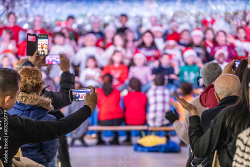 Families enjoying the Christmas festival at their children's school, father videotaping with his phone, unrecognizable people and out-of-focus background
