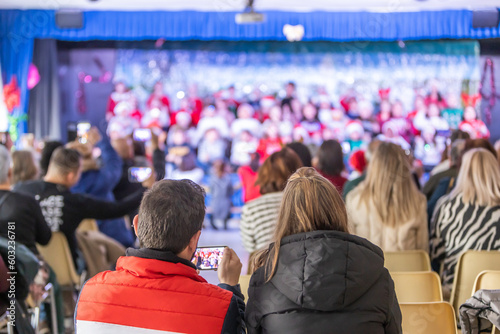 Families enjoying the Christmas festival at their children's school, father videotaping with his phone, unrecognizable people and out-of-focus background