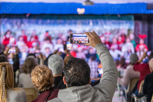 Families enjoying the Christmas festival at their children's school, father videotaping with his phone, unrecognizable people and out-of-focus background
