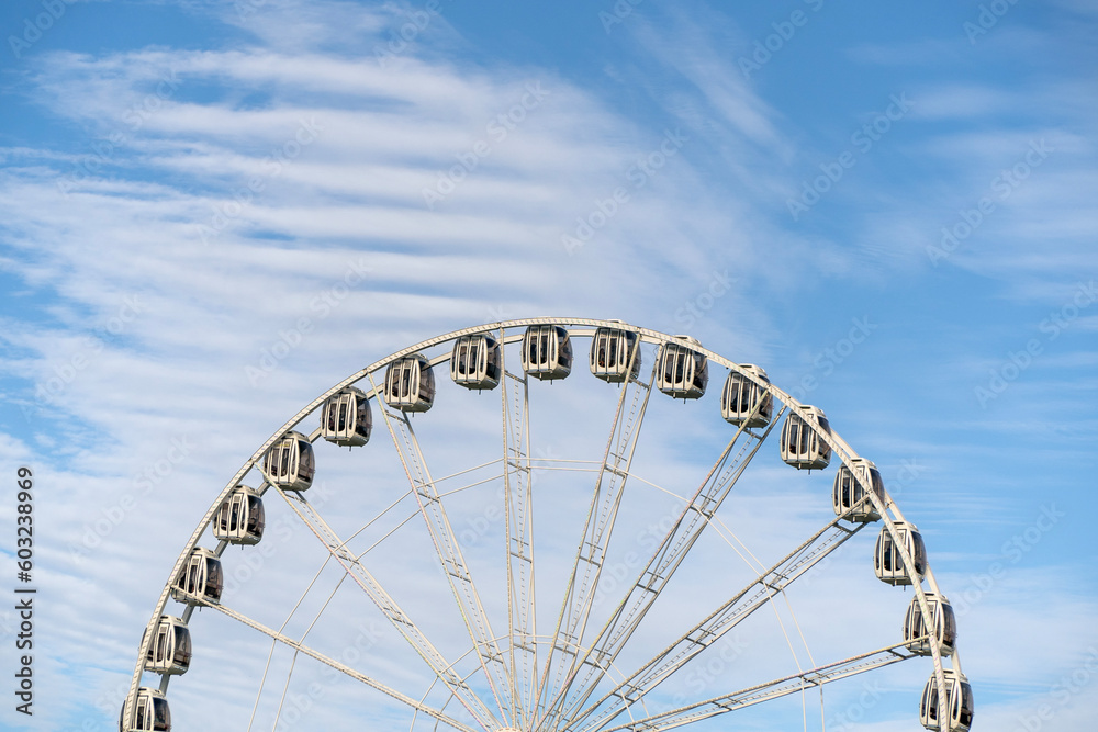 A view of a the top half of a Ferris Wheel against to cloudy sky.